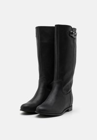 Bottes noires à hauteur de genou en cuir, présentant une texture lisse, un léger talon et un accent décoratif en tresse sur le côté.
