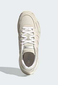 Ljusbeige sneaker med ovandel av mesh och mocka, med vita snören och en dämpad sula. Diskret logga på tungan och sidan.