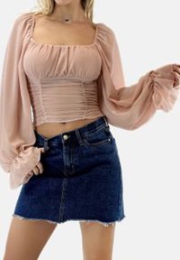 Top de manga larga de color rosa claro con fruncidos, combinado con una minifalda de mezclilla oscura con dobladillo deshilachado. Tela texturizada y diseño ajustado.