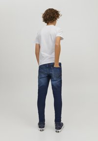 Jeans in denim blu con vestibilità slim, indossati con una t-shirt bianca a maniche corte. Presentano tasche posteriori con dettagli di cucitura discreti.