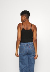 Svart tettsittende tanktopp med tynne stropper kombinert med høyt liv blå denimjeans med baklommer og et lite logo-merke.