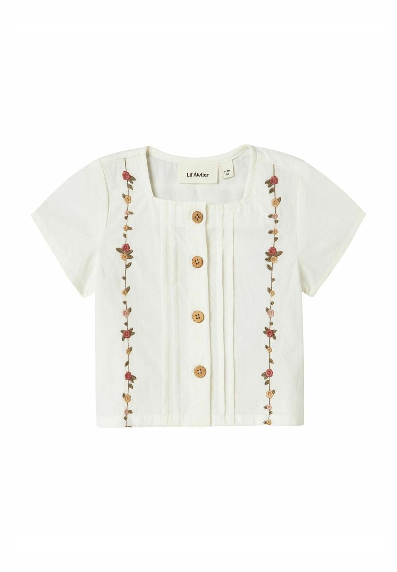 Blusa bianca a maniche corte con scollo quadrato, bottoni in legno e ricami floreali sul davanti. Tessuto leggero con pieghe.