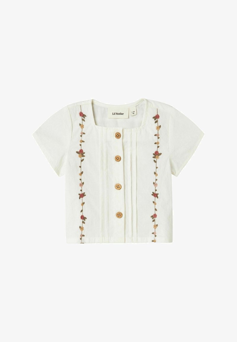 Blusa bianca a maniche corte con scollo quadrato, bottoni in legno e ricami floreali sul davanti. Tessuto leggero con pieghe.