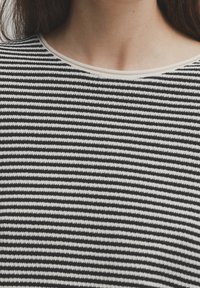 Maglione a righe bianche e nere con scollo rotondo e rifiniture chiare a contrasto. Texture morbida, righe orizzontali e materiale di peso medio.