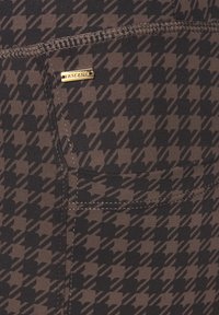 Brown fabric with a houndstooth pattern, featuring a gold hardware accent and contrasting white stitching, viewed from a close angle.