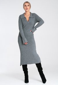 Szara dzianinowa sukienka w prążki z kołnierzykiem, długimi rękawami i dopasowanym fasonem sięgającym kostek. Faktura wydaje się miękka i elastyczna.