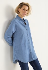 Hellblaues Denimhemd mit langen Ärmeln, Knopfleiste und abgerundetem Saum. In Kombination mit dunklen Jeans hat es eine lockere Passform und einen Kragen.