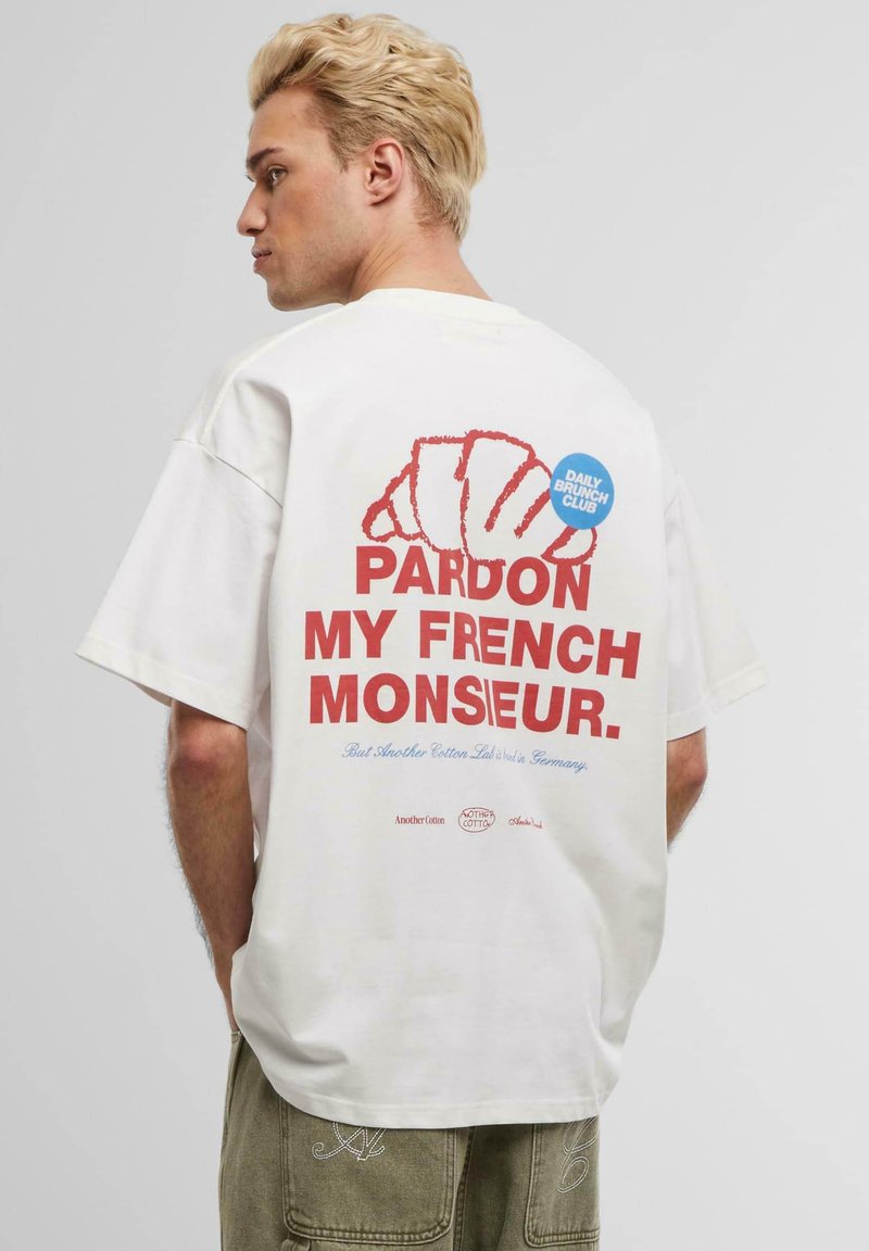White oversized cotton t-shirt featuring red and blue text on the back, a croissant graphic, and "DAILY BRUNCH CLUB" badge.