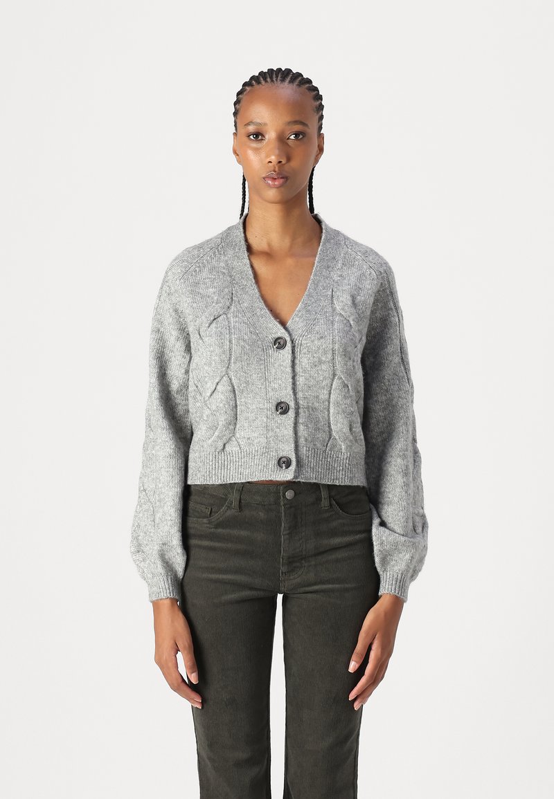 Gray cropped cardigan with a V-neck, ribbed cuffs, textured cable knit pattern, and three dark buttons. Paired with dark green corduroy pants.