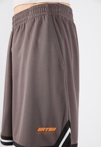 Shorts de sport gris en tissu en maille texturée, avec une taille élastique, des accents noirs et un logo "URTRD SPORT" orange.
