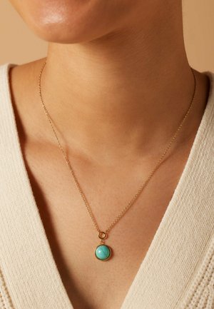 Goldfarbener Halsreifen mit einem runden, türkisfarbenen Anhänger. Der Anhänger hat eine glatte Oberfläche und ist in einem schlichten Rahmen eingefasst. Die Kette ist zart und dünn.