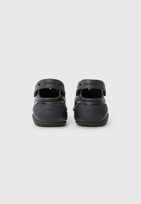 Black Crocs clogs with a smooth rubber material, adjustable heel strap, and vent holes on the sides for breathability.