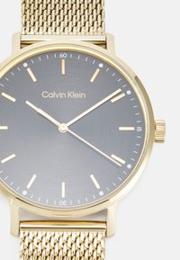 Gold Mesh-Uhrenarmband mit einem grauen Zifferblatt, goldenen Stundenmarkierungen und Zeigern. Verfügt über ein minimalistisches Design mit einer polierten Oberfläche und Logo.