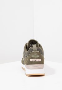 Olijfgroene sneaker met een gestructureerde stof en een suède afwerking. Voorzien van een stevige zool, een roze logo en zichtbare stiksels aan de achterkant.