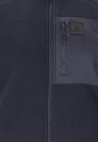 Marine fleece jack met een rits borstzak en een gladde stoffen paneel. Inclusief een logo patch aan de bovenste linkerzijde.