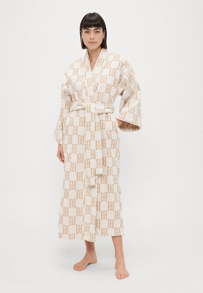 Pikk, beež mantel kergete pruunide geomeetriliste mustritega, valmistatud pehmest ja tekstuurses materjalis, vöödiga talje ja laiad varrukad.