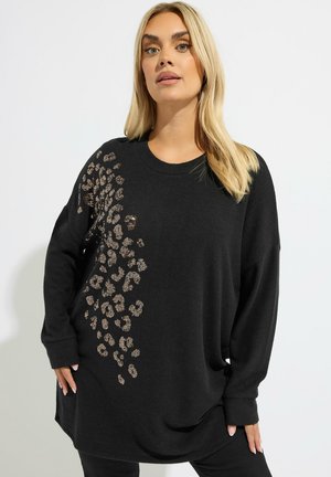 Pull oversized noir en tissu doux avec un motif léopard et des accents métalliques dorés d'un côté. Il présente un col rond et des manches longues.