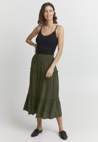 Camisola nera con pizzo abbinata a una gonna maxi a più strati di colore verde oliva. Il tessuto sembra morbido, con dettagli arricciati all'orlo.