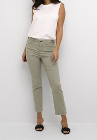 Top sin mangas de color gris claro combinado con pantalones rectos de color verde claro y sandalias negras tipo deslizante. Tejido suave con un ajuste relajado y detalles mínimos.