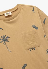 Camiseta de manga corta beige hecha de algodón, con patrones de palmeras y piñas en azul marino, y un detalle de bolsillo en el pecho.