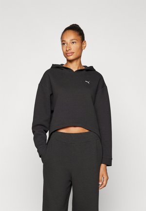 Haut à capuche noir cropped avec un motif texturé, doté d'une capuche à cordon et d'un logo blanc. Associé à un pantalon de survêtement noir texturé assorti.