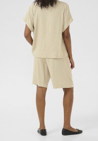 Top beige a maniche corte e pantaloni corti coordinati realizzati in un tessuto leggero, con una vestibilità morbida e una superficie liscia. Ballerine nere completano il look.