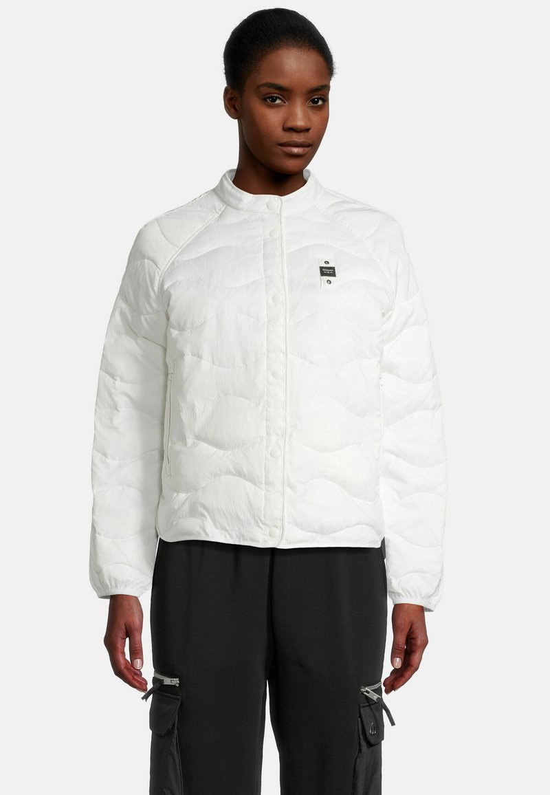 Veste blanche rembourrée avec un col rond, fermeture à boutons-pression et un petit logo sur la poitrine. Texture lisse avec des détails matelassés.