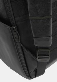 Zaino nero con un pannello in pelle testurizzata, molteplici zip e hardware per cinghie regolabili; finitura opaca con accenti lisci.
