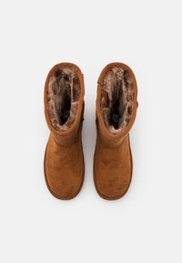 Hnědé semišové kotníkové boty s měkkou kožešinovou podšívkou. Zaoblená špička a prošívané detaily kolem kotníku. Žádné viditelné hardware nebo akcenty.