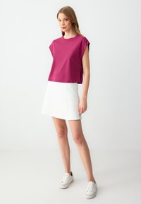 T-shirt magenta a maniche arrotolate, abbinato a una mini gonna bianca e sneakers bianche. Tessuto morbido e design semplice.