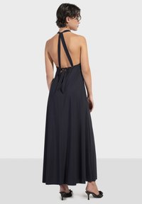 Crna halter maxi haljina s otvorenim leđima učvršćena vezicama, lepršavom tkaninom i opuštenim krojem koji seže do gležnjeva.