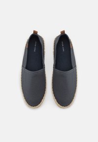 Grå lerret slip-on sko med avrundet tå, jute tau detaljer langs sålen, og en tan skinn aksent ved hælen.