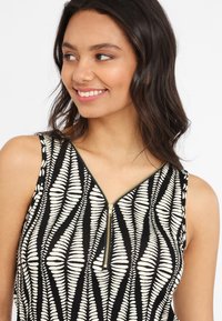 Top sans manches noir et blanc à motif, avec un col zippé, de texture lisse et un motif en forme de feuille.