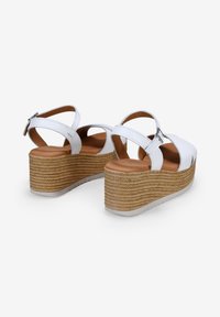 Sandalias de cuña blancas con material superior texturizado, correas en el tobillo y una media suela de yute trenzado con una suela de goma ligera.