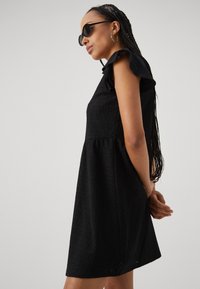 Vestido preto com mangas curtas e bufantes, apresentando um tecido texturizado e um corpete ajustado que se alarga numa saia solta.