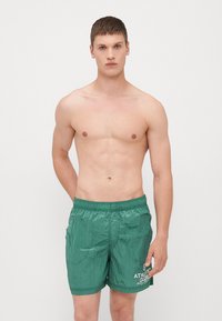 Zöld fürdőshorts könnyű anyagból, rugalmas derékkal és fehér "ATHLETIC CLUB" felirattal a bal lábon.