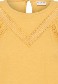 Mustár sárga felső V-alakú csipkedíszítéssel a kerek nyakkivágás közelében és Pulz Jeans címkével a gallér belsejében.