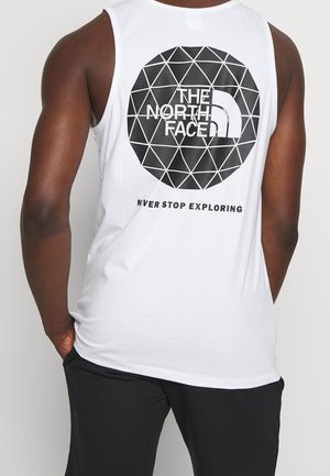 Mężczyzna w białej koszulce bez rękawów z czarnym geometrycznym logo w kształcie koła oraz napisem "THE NORTH FACE" i "NEVER STOP EXPLORING" na plecach.