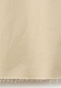 Tissu beige avec un motif de tissage diagonal et un bord effiloché en bas.