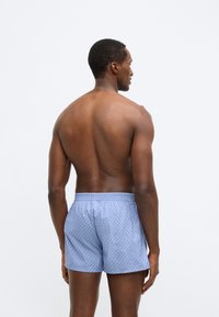 Μπλε μαγιό με σχέδια από ελαφρύ ύφασμα, με ελαστική μέση και άνετη εφαρμογή, εμφανιζόμενο από την πίσω όψη.