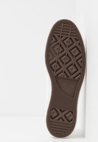 Suola di scarpa in gomma marrone con pattern geometrici testurizzati, che presenta il logo "Converse ALL STAR" e le marcature della taglia. Sono visibili costole verticali e orizzontali.