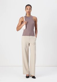 Ljusbrun ribbad linne, beige vida byxor och svarta klackar. Modellen håller en liten rosa handväska. Minimalistisk design och färger.
