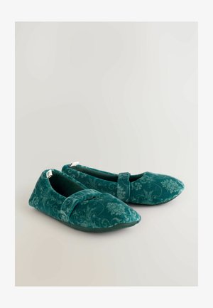 Une paire de pantoufles plates en velours teal avec des motifs floraux et une sangle sur le dessus, placées sur un fond clair.