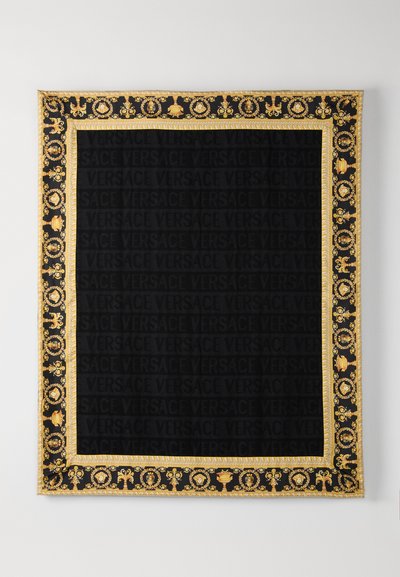 Czarna tkanina ze złotą, ozdobną ramką i wzorem z napisem „VERSACE”. Elementy dekoracyjne obejmują urny i motywy kwiatowe. Elegancki design.