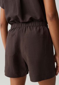 Person wearing dark brown shorts with elastic waistband and two back pockets, shown from the waist to mid-thigh.