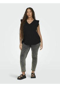 Crna majica s v-izrezom i naboranim rukavima, u kombinaciji s sivim trapericama s blagim istrošenim efektom i crnim platformama.