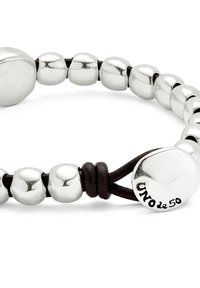 Pulsera de cuentas de plata con cuentas metálicas redondeadas y pulidas y un cordón de cuero oscuro. Un detalle notable incluye el logo grabado en una de las cuentas.