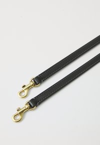 Δύο μαύρα δερμάτινα λουριά με χρυσά μεταλλικά περιστρεφόμενα κρίκους σε άσπρο φόντο.