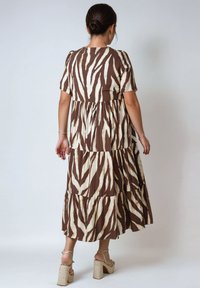 Brown and cream tiered maxi dress featuring a zebra stripe pattern, short sleeves, and a relaxed fit. Worn with strappy beige heels.