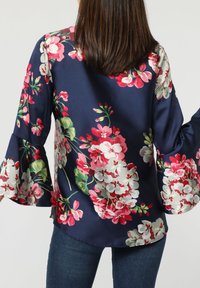 Blusa navy con un patrón floral en rosa y blanco. Presenta mangas de campana y una tela suave y brillante. Ajuste casual con un dobladillo redondeado.
